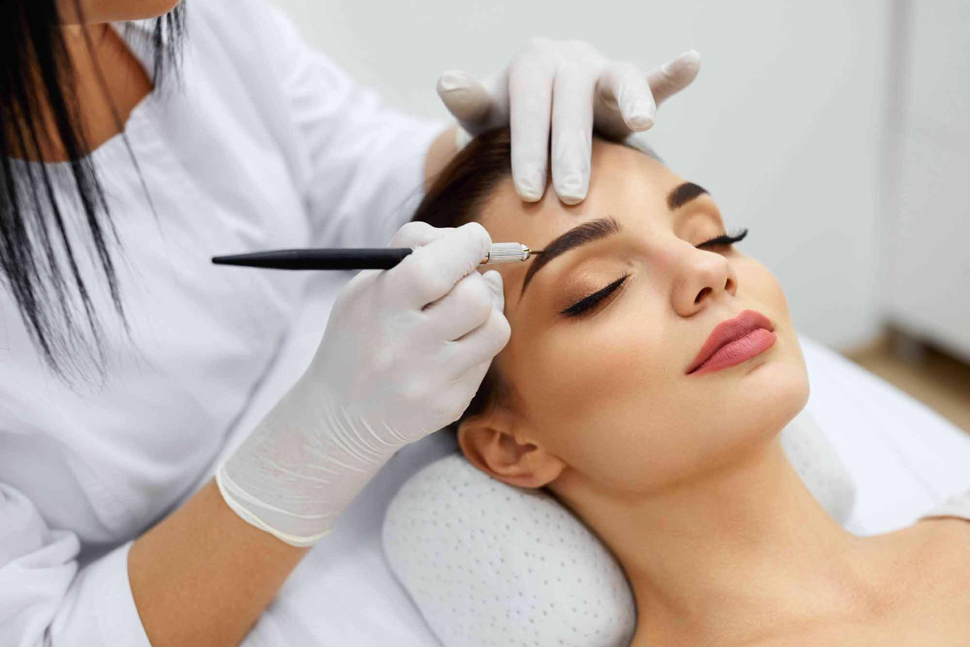 Kosmetikerin, die dauerhafte Augenbrauen-Make-uptätowierung auf Frauengesicht platziert