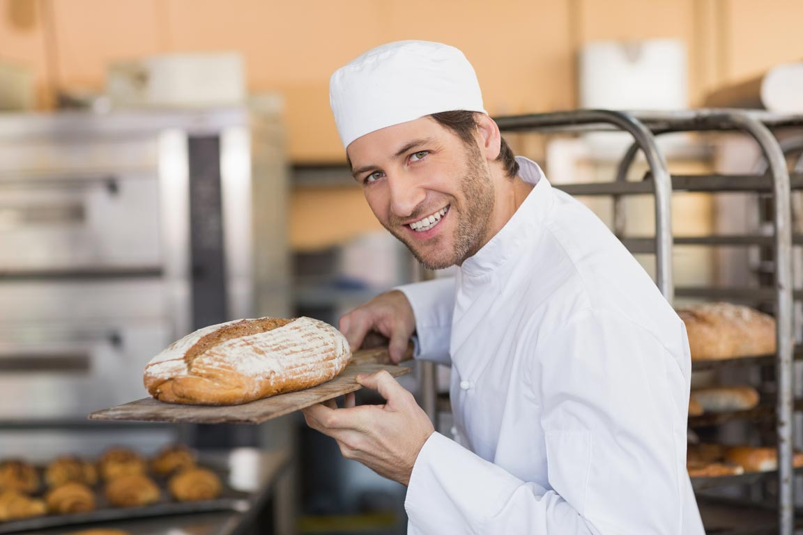 Bäcker in der Backstube mit einem selbst gebackenen Brot auf dem Blech.