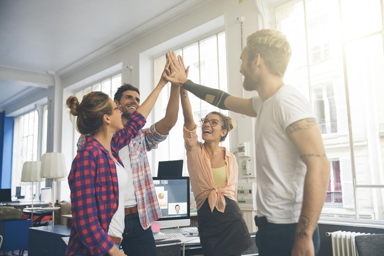 4 junge Erwachsene die sich ein Gruppen High-Five in einem Büro geben